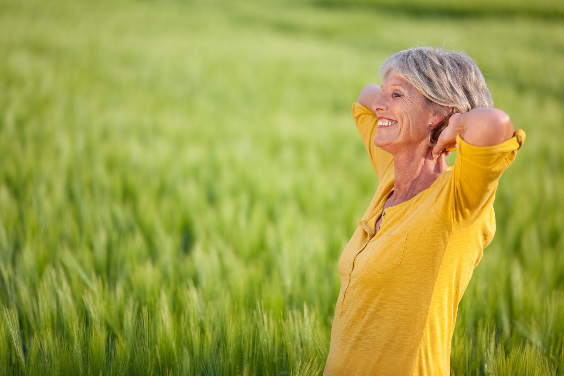 Senior Woman With Hands Behind Head On Grassy Field