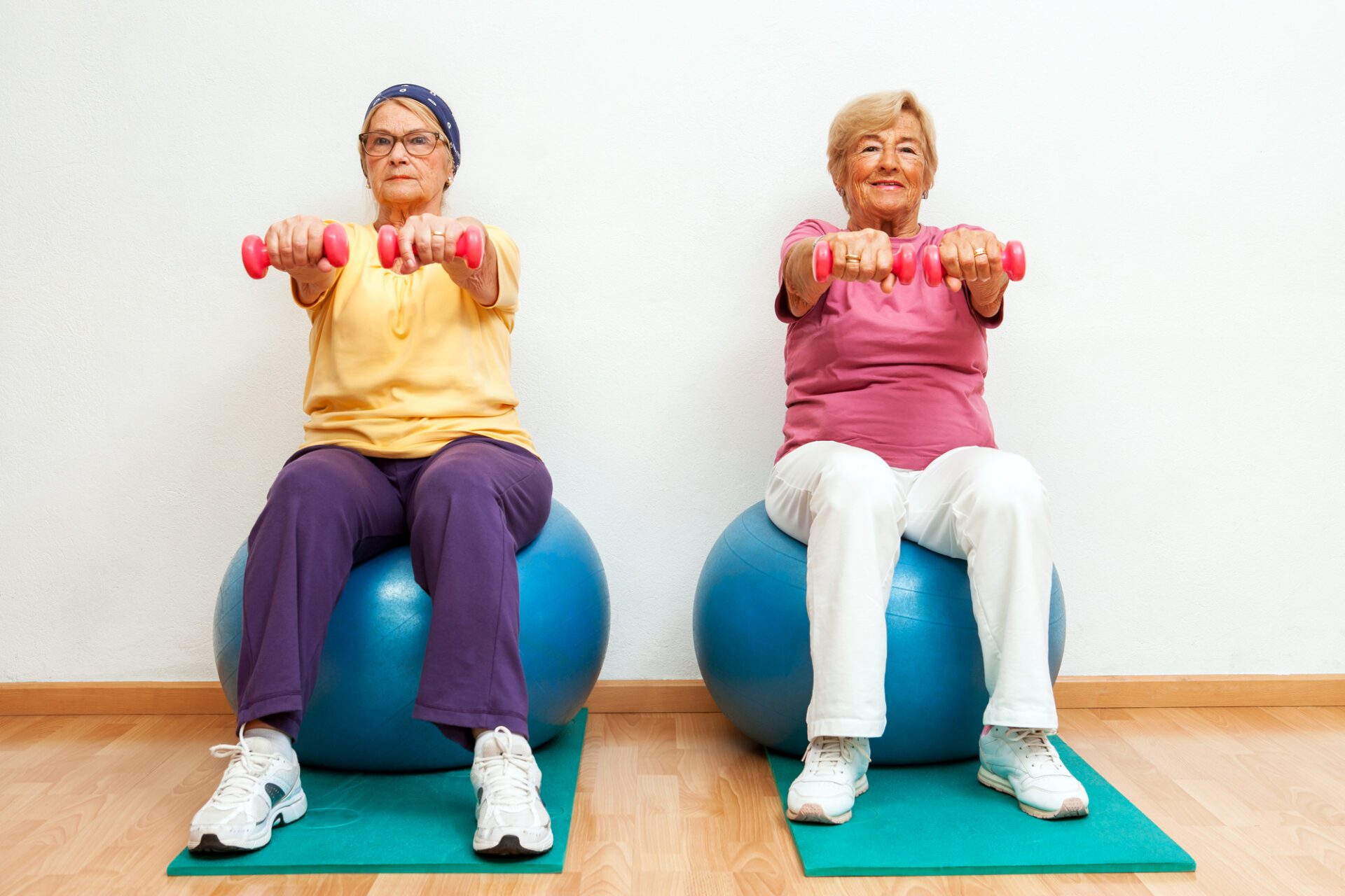 Two elderly women doing muscle exercises with weights in gym.