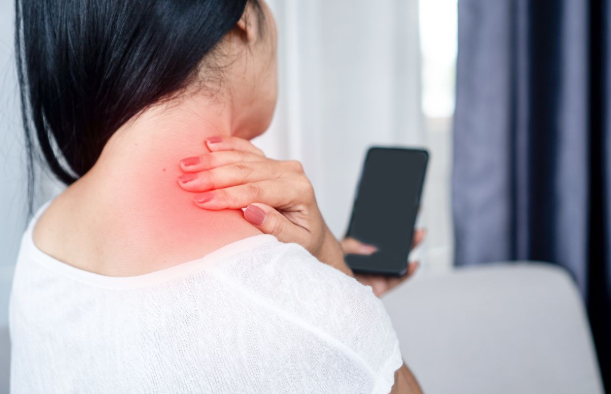 Woman experiencing neck pain while using her cellphone